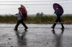 Workers, wearing face masks to protect against coronavirus, hold umbrellas as they walk home from work in Kwa-Thema, east of Johannesburg, South Africa, April 1, 2020.