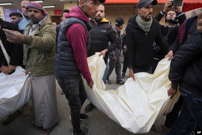 Warga Palestina membawa karung putih berisi jenazah korban tewas dalam serangan udara Israel semalam di kamp pengungsi Maghazi, di Rumah Sakit Al-Aqsa, di Deir al-Balah, bagian tengah Jalur Gaza, 28 Desember 2024. (Foto: AP)