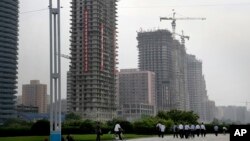 In this June 27, 2016, photo, North Korean men cycle, while others walk past buildings under construction on “Ryomyong Street,” in Pyongyang, North Korea. Leadership is hoping to show the world the country is doing just fine despite sanctions and outside pressure over its nuclear weapons program.