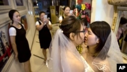 FILE - Teresa Xu, left, and Li Tingting, right, share a kiss as clerks take photographs in a beauty salon where the two were preparing for their wedding in Beijing, July 2, 2015.