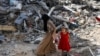 Una mujer y una niña caminan entre los escombros, después de los ataques israelíes en el área donde los rehenes israelíes fueron rescatados el sábado, en el campo de refugiados de Nuseirat en el centro de la Franja de Gaza, el 9 de junio de 2024. 