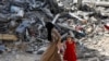 一名巴勒斯坦妇女和儿童在加沙中部努塞拉特难民营的废墟中行走。（2024年6月9日）