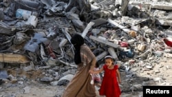 Seorang perempuan dan anak-anak berjalan di antara reruntuhan bangunan di kamp pengungsi Nuseirat di Gaza tengah, pada 9 Juni 2024. Bangunan kamp hancur akibat serangan Israel ke area tersebut. (Foto: Reuters/Abed Khaled)