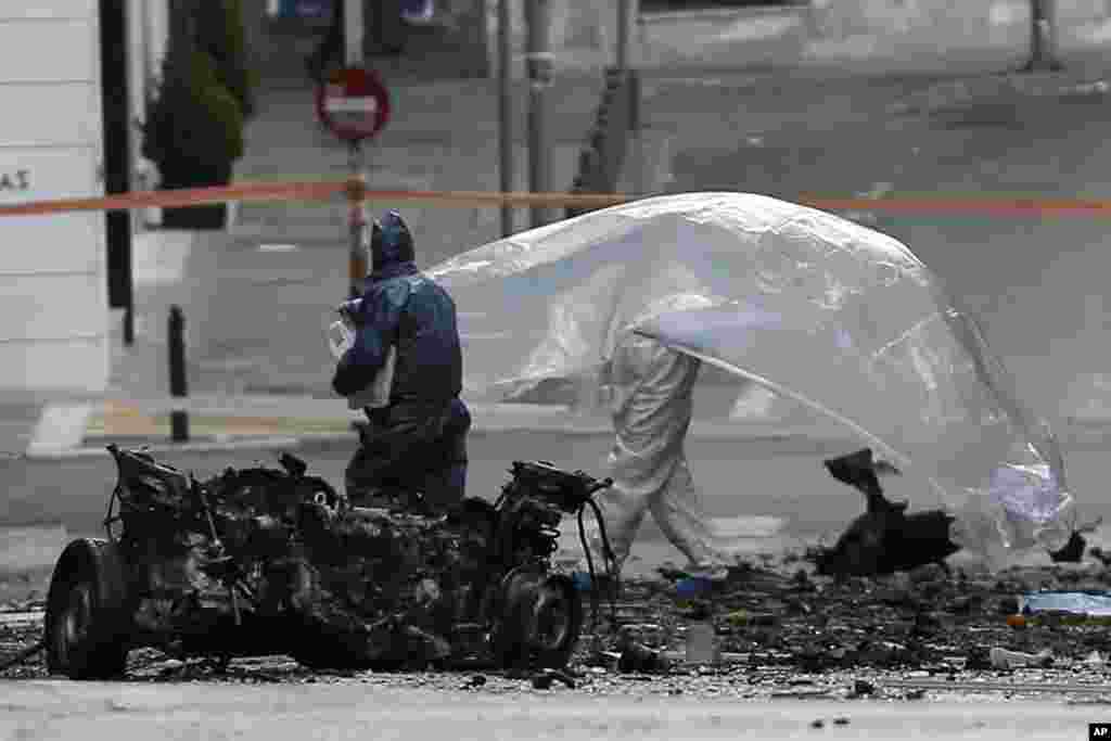 Police bomb disposal experts place plastic sheeting over the remains of a car bomb that exploded in central Athens, April 10, 2014. 