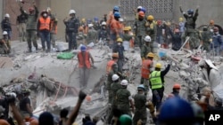 Rescue workers, some holding their arms up as a sign to maintain silence, search for survivors at an apartment building at Amsterdam and Laredo streets that collapsed during an earthquake in the Condesa neighborhood of Mexico City, Mexico, Sept. 21, 2017.