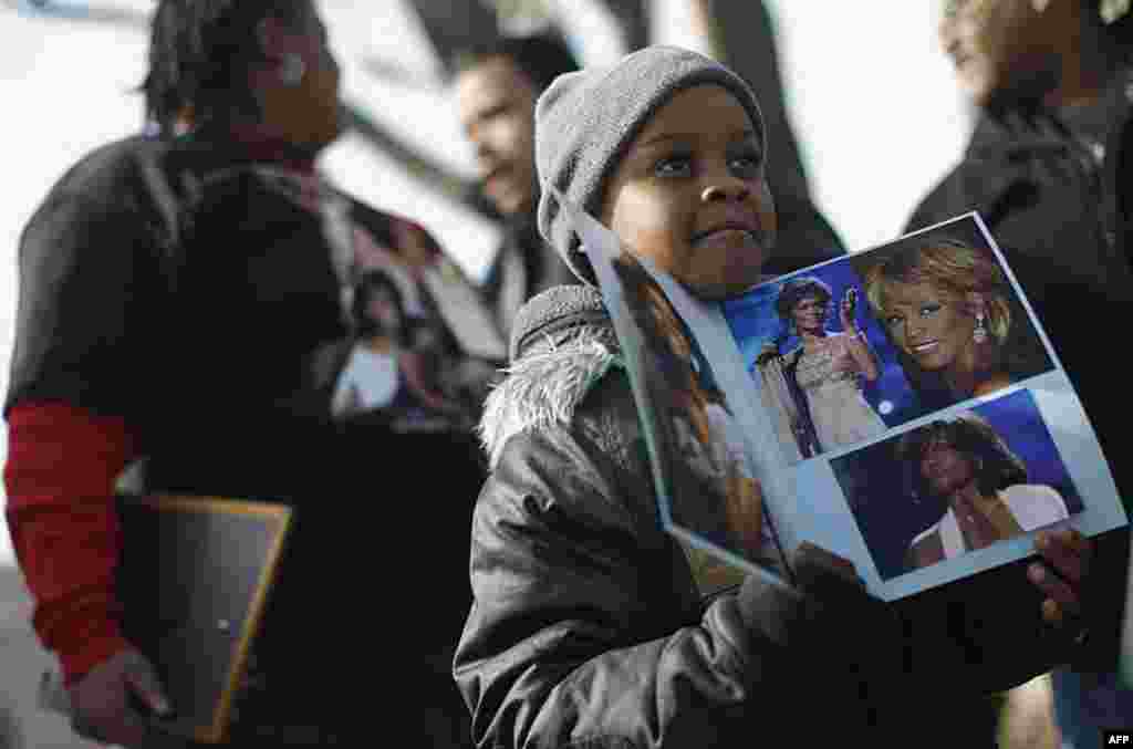 A young boy holds photographs Whitney Houston during the funeral service for the late singer near the New Hope Baptist Church, Newark, New Jersey, February 18, 2012. (REUTERS)