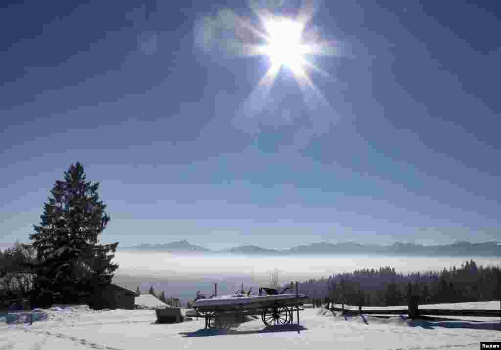 A snow-covered horse carriage is pictured on top of the Taubenberg mountain while fog dissipates under the early morning sun in Warngau, Germany. 