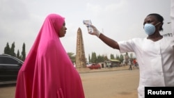 Seorang petugas memeriksa suhu tubuh seorang warga di Abuja, Nigeria, 30 Maret 2020. (Foto: dok). 