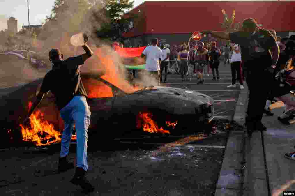 People react as a car burns at the parking lot of a Target store during protests after a white police officer was caught on a bystander&#39;s video pressing his knee into the neck of African-American man.