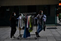 Two workers of clothes shop wearing face mask protections to prevent the spread of the coronavirus, pull a rack of clothes along a street, in Pamplona, northern Spain, May 11, 2020.