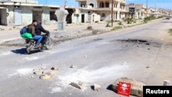 Dua orang pria dengan sepeda motornya melewati papan peringatan bertuliskan "Awas, Amunisi (Bahan Peledak)" pada lokasi yang diperkirakan mendapat serangan senjata kimia, di daerah Khan Sheikhoun, Idlib, Suriah yang dikuasai pemberontak, 5 April 2017. (REUTERS/Ammar Abdullah)