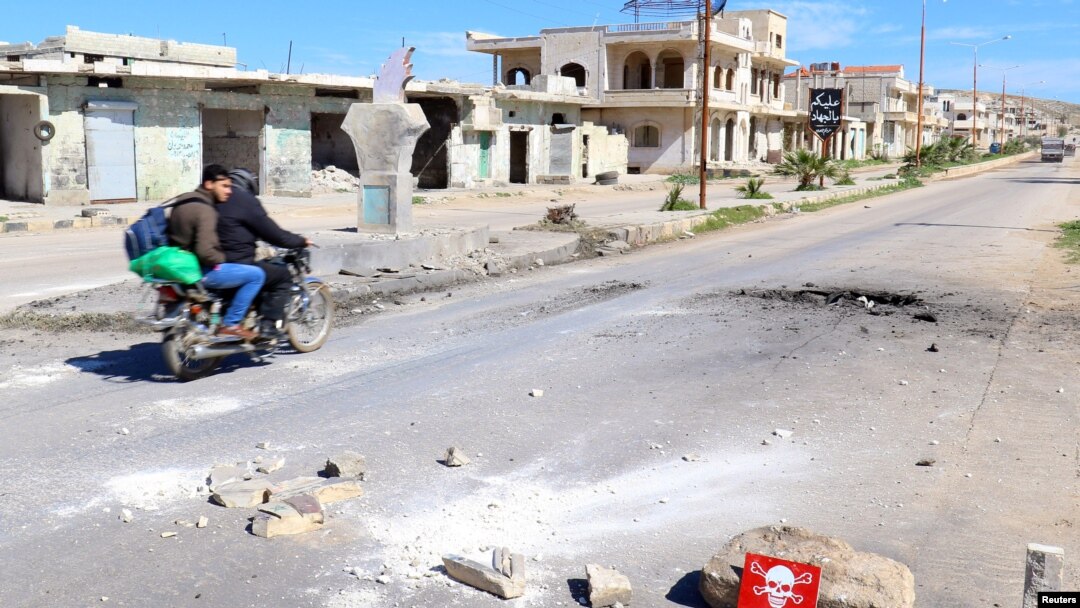 Beberapa pria mengendarai sepeda motor melewati tanda bahaya di lokasi yang dihantam serangan udara baru-baru ini di kota Khan Sheikhoun di provinsi Idlib yang berada di bawah kendali pemberontak, tanggal 5 April 2017 (foto: REUTERS/Ammar Abdullah)