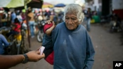An elderly woman is offered cash as she begs at a wholesale food market in Caracas, Venezuela, Monday, Jan. 28, 2019. (AP Photo/Rodrigo Abd)