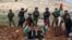 File - Palestinians hold flag in front of Israeli forces during clashes as they protest against Israeli Jewish settlements, in the village of Beit Dajan near the West Bank city of Nablus, Nov. 27, 2020.