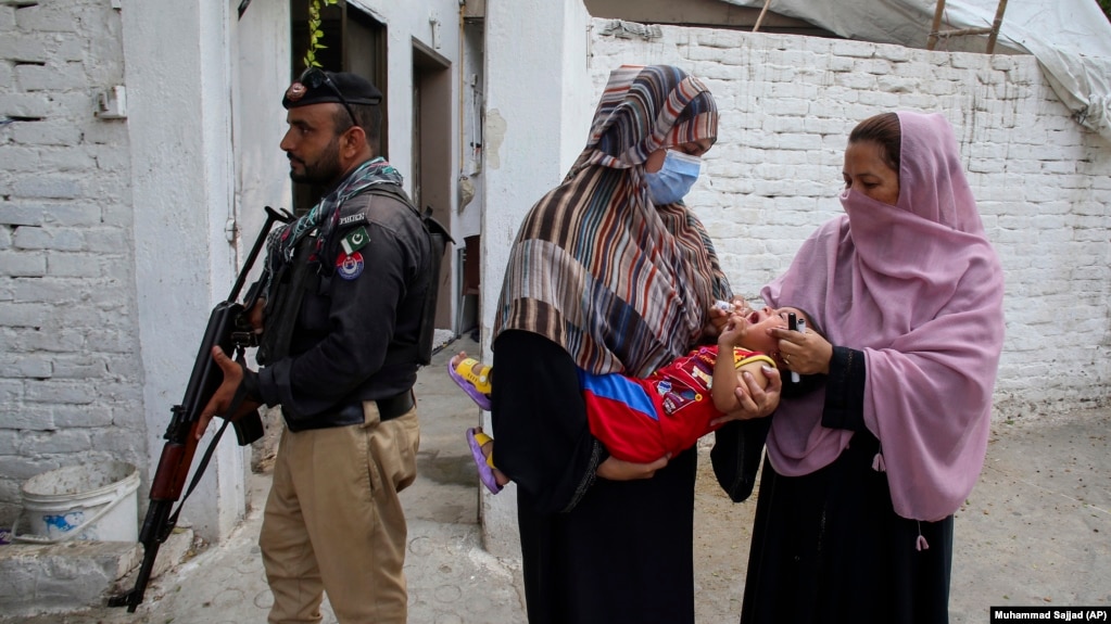 A police officer stands guard as a health worker, right, gives a polio vaccine to a child in a neighborhood of Peshawar, Pakistan, September 9, 2024. (AP Photo/Muhammad Sajjad)