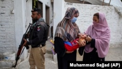 A police officer stands guard as a health worker, right, gives a polio vaccine to a child in a neighborhood of Peshawar, Pakistan, September 9, 2024. (AP Photo/Muhammad Sajjad)