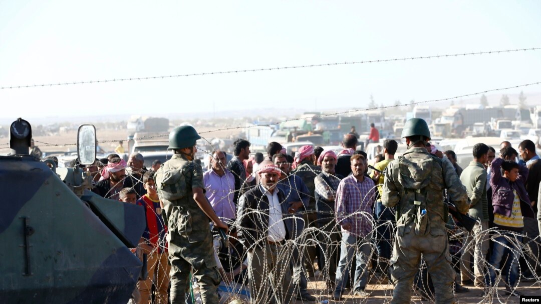 Tentara Turki bersiaga saat para pengungsi Kurdi dari Suriah menunggu di belakang sebuah pagar perbatasan dekat kota Suruc di sebelah tenggara provinsi Sanliurfa, Turki (22/9). 