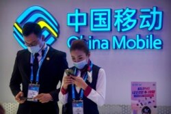 FILE - Staff members wearing face masks to protect against the spread of the coronavirus use their smartphones at a display from Chinese telecommunications firm China Mobile at the PT Expo in Beijing, Oct. 14, 2020.