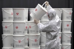 A worker in protective gear stacks plastic buckets containing medical waste from coronavirus patients at a medical center in Daegu, South Korea, Feb. 24, 2020.