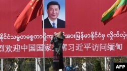 Seorang perempuan menyiram taman di depan papan ucapan selamat datang untuk Presiden China Xi Jinping, di Naypidaw, Myanmar, 17 Januari 2020. (Foto: AFP)