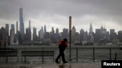 Seorang pria berjalan di tengah hujan deras dan angin di Weehawken, New Jersey, AS, di sepanjang tepi Sungai Hudson dengan latar belakang gedung pencakar langit Kota New York, saat kawasan tersebut diterpa Badai Tropis Isaias, 4 Agustus 2020. (REUTERS/Mike Segar)