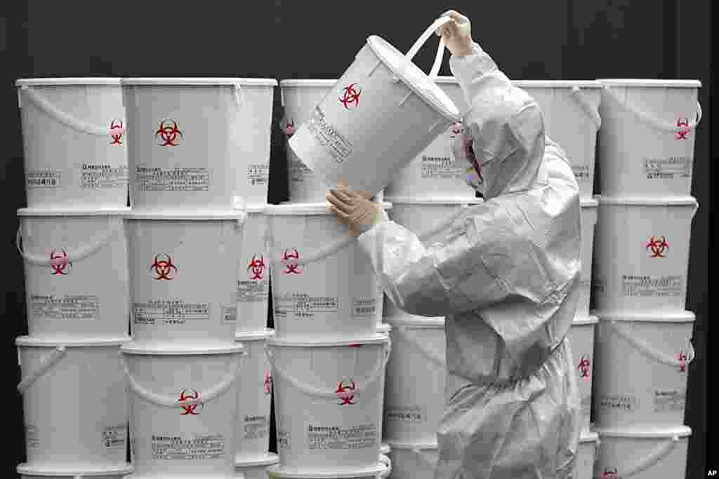 A worker in protective gear stacks plastic buckets containing medical waste from coronavirus patients at a medical center in Daegu, South Korea.
