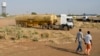 FILE - Two men walk near the Paloch oil fields in Upper Nile State, the site of an oil complex and key crude oil processing facility in the north of the country near the border with Sudan. 