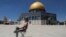 A masked Palestinian demonstrator holds a stone during clashes with Israeli security forces in front of the Dome of the Rock Mosque at the Al Aqsa Mosque compound in Jerusalem's Old City.
