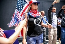 (FILES) In this file photo taken on May 01, 2020 conspiracy theorist QAnon demonstrators protest during a rally to re-open California and against Stay-At-Home directives in San Diego, California. - YouTube said October 15, 2020 it was tightening…