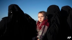 Seorang wanita menggendong seorang anak saat dia menunggu untuk diperiksa Pasukan Demokratik Suriah (SDF) yang didukung AS di gurun di luar Baghouz, Suriah, 1 Maret 2019. (Foto: AP)