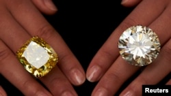 Seorang model memamerkan cincin berlian warna kuning sebesar 100,09 karat (kiri) dan cincin berlian 103,46 karat dalam sebuah lelang di Sotheby's di Jenewa, 7 Mei 2014. (Foto: dok.) 