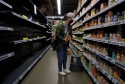 A woman wearing a face mask and gloves buys canned foods beside empty shelves, at a supermarket in Hong Kong, Feb. 13, 2020.