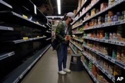 A woman wearing a face mask and gloves buys canned foods beside empty shelves, at a supermarket in Hong Kong, Feb. 13, 2020.