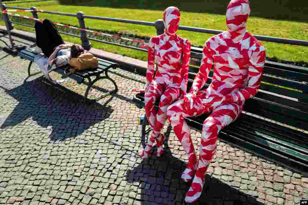 A woman takes a nap on a bench next to mannequins wrapped in barrier tape near Berlin&#39;s landmark Brandenburg Gate as part of German artist Dennis Josef Meseg&#39;s Corona Memorial called &quot;It is Like it is.&quot;