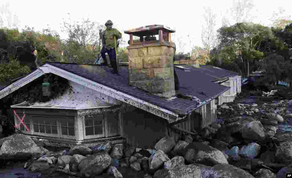 A firefighter stands on the roof of a house submerged in mud and rocks in Montecito, California.