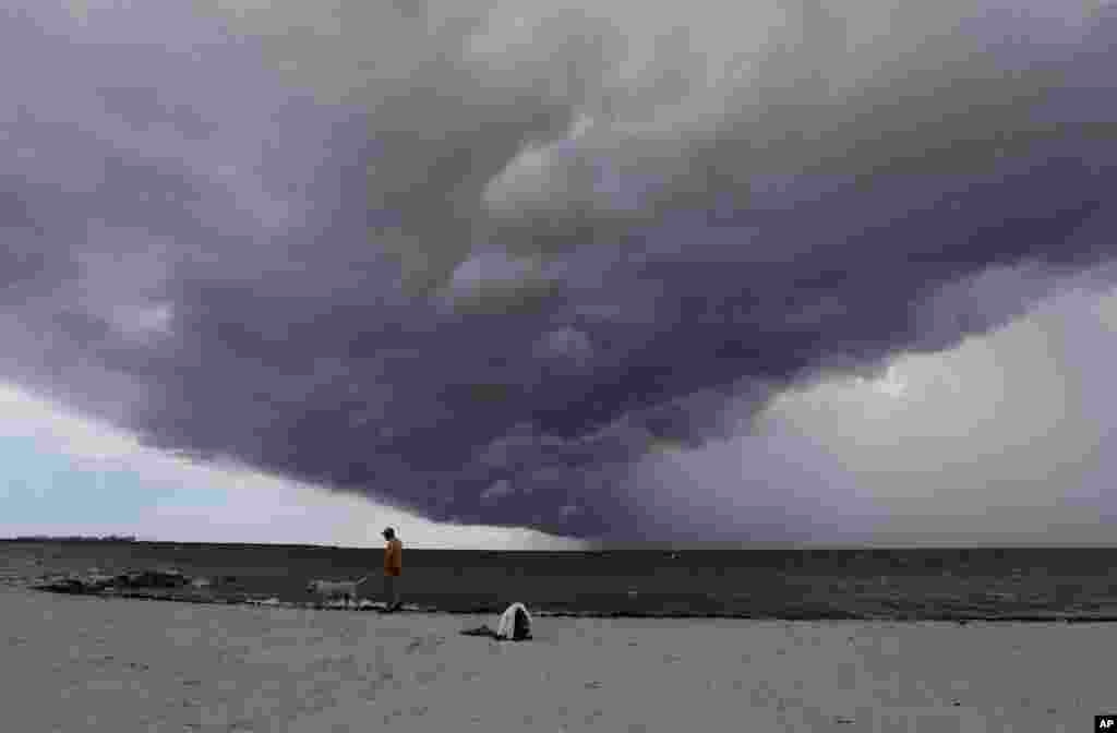 Arnie Powell walks along the beach with his pet dog, Biscuit, as rain clouds approach Hobie Beach in Key Biscayne, Florida, July 22, 2015.