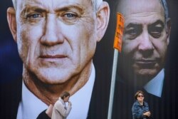 People walk by an election campaign billboard for the Blue and White party, the opposition party led by Benny Gantz, left, in Ramat Gan, Israel, Feb. 20, 2020. Prime Minister Benjamin Netanyahu of the Likud party is pictured at right.
