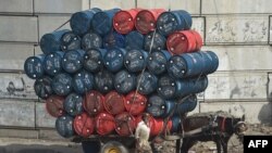 A man stands next to a horsecart laden with oil drums on a street in Lahore, Pakistan.
