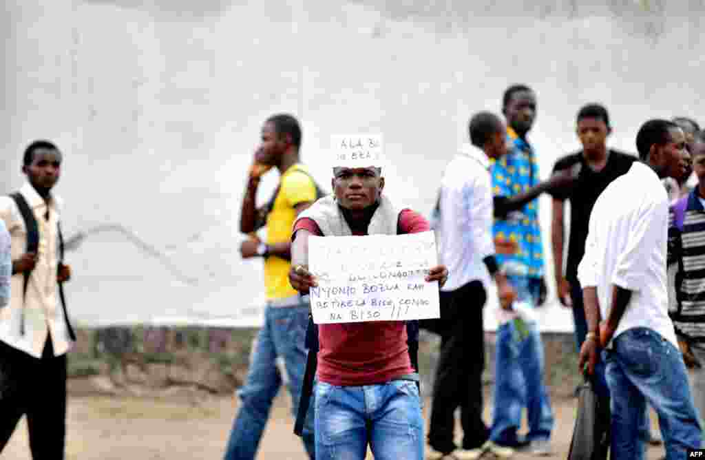 A student from the Architecture and Urbanism institute holds a sign protesting against civil unrest outside of their university in Kinshasa. The sign reads: "Too much is too much. What do you want with the Congo."