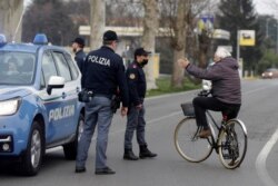 A cyclist talks to police officers controlling movements to and from the cordoned area in Casalpusterlengo, Northern Italy, Feb. 23, 2020.