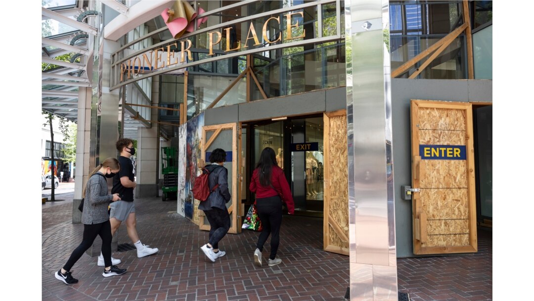 Shoppers walk into Pioneer Place shopping mall, which is still protected by wooden panels to prevent windows being smashed by ongoing protests in Portland, Ore., on June 5, 2021.