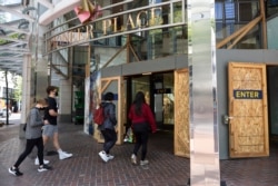 Shoppers walk into Pioneer Place shopping mall, which is still protected by wooden panels to prevent windows being smashed by ongoing protests in Portland, Ore., on June 5, 2021.
