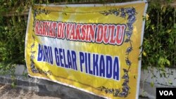 Spanduk bertuliskan desakan memprioritaskan vaksinasi daripada Pilkada terpasang di salah satu persimpangan jalan di Solo, beberapa waktu lalu. (Foto: VOA/ Yudha Satriawan)