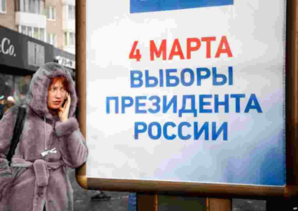 A woman wearing a white ribbon -- the symbol of recent protests against fraudulent elections -- stands beside an informational poster for the upcoming March 4 presidential elections, February 4, 2012. (VOA - Y. Weeks)