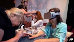 In this Tuesday, Aug. 6, 2019, photo, Kohler Waters Spa cosmetologist Jodi Gerk, left, performs a virtual reality manicure at the 2019 International Spa Association event, in New York. (AP Photo/Richard Drew)