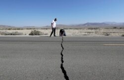 FILE - Two men examine a crack caused by an earthquake on State Route 178 outside of Ridgecrest, Calif., July 6, 2019.
