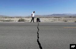FILE - Two men examine a crack caused by an earthquake on State Route 178 outside of Ridgecrest, Calif., July 6, 2019.