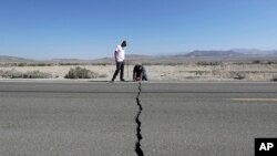 FILE - Two men examine a crack caused by an earthquake on Highway 178 outside of Ridgecrest, Calif., July 6, 2019. 