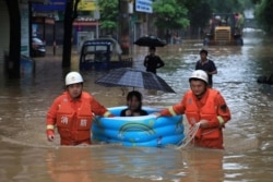 Rescue workers wade through flood waters as they evacuate a woman with an inflatable swimming pool following heavy rainfall in Pingxiang, Jiangxi province, China, July 9, 2019.