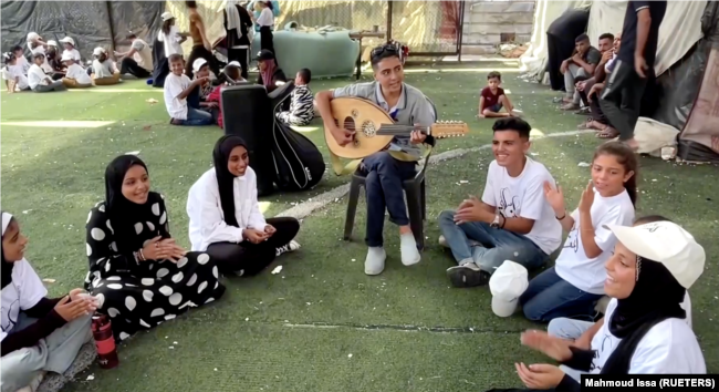 In this frame captured from video, Palestinian teenager Youssef Saad plays the oud and sings to children amid Israel-Hamas conflict, in Jabalia refugee camp in the northern Gaza Strip September 2, 2024. (REUTERS/Mahmoud Issa)